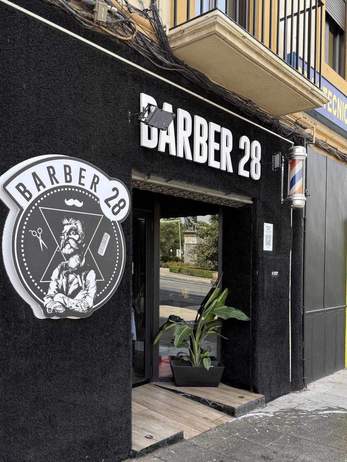Fachada del local de Granada Centro: rótulo BARBER 28 en letras blancas sobre pared negra, el emblema de la casa y un poste de barbero junto a la puerta